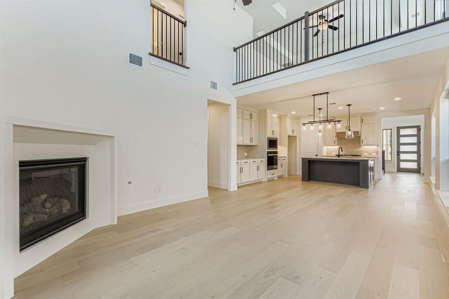 Unfurnished living room featuring a ceiling fan, light wood-style floors, a towering ceiling, and a glass covered fireplace Unfurnished living room featuring a ceiling fan, light wood-style floors, a towering ceiling, and a glass covered fireplace