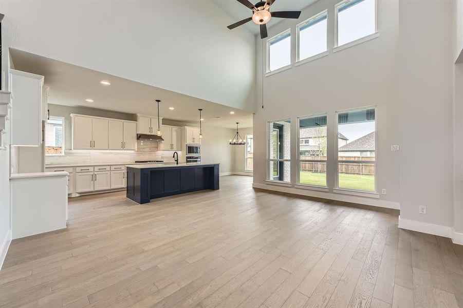 Kitchen with a sink, a ceiling fan, a high ceiling, under cabinet range hood, and light countertops