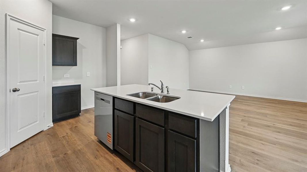 Kitchen featuring stainless steel dishwasher, light wood-style flooring, a center island with sink, recessed lighting, and light stone counters