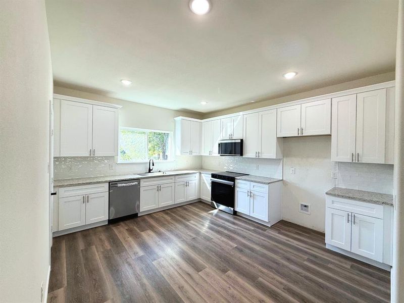 Kitchen with appliances with stainless steel finishes, white cabinets, tasteful backsplash, dark wood-style flooring, and recessed lighting
