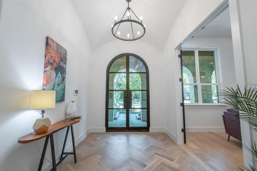 Entrance foyer featuring french doors, vaulted ceiling, a notable chandelier, and light parquet flooring