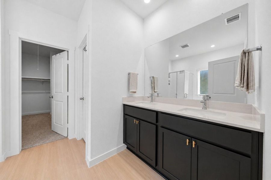 A light-filled primary bathroom showcases a dual vanity, sleek modern finishes, and a large statement mirror, with direct access to a generously sized walk-in closet.