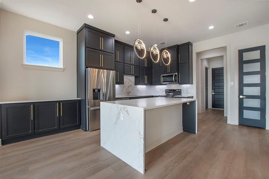 Kitchen with a center island, hanging light fixtures, decorative backsplash, light hardwood / wood-style floors, and stainless steel appliances