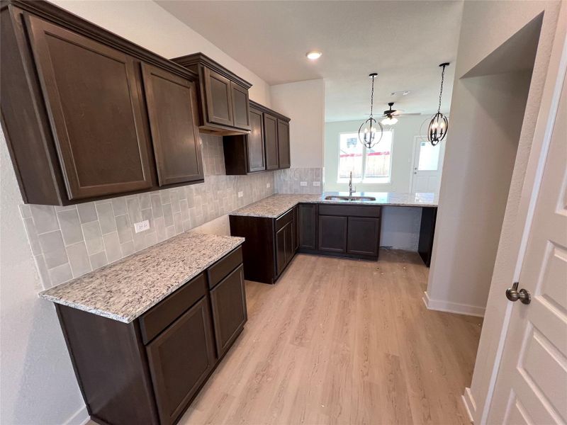 Kitchen with dark brown cabinetry, backsplash, light stone countertops, and recessed lighting
