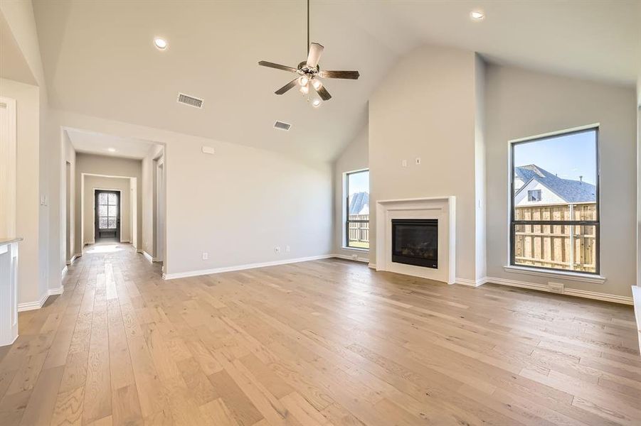 Unfurnished living room featuring high vaulted ceiling, light hardwood / wood-style flooring, ceiling fan, and a healthy amount of sunlight