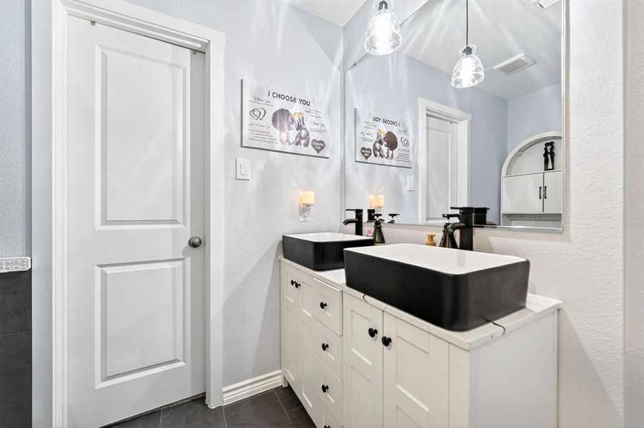 Dual vessel sinks with matte black fixtures atop a white vanity, reflecting pendant lighting