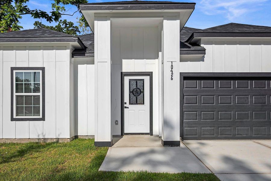 Modern white facade with sleek black accents, featuring a stylish front door and attached garage, set against a well-maintained lawn.