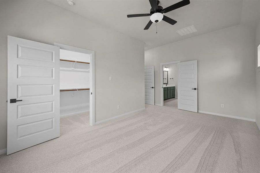 Unfurnished bedroom featuring light carpet, a walk in closet, ceiling fan, and connected bathroom