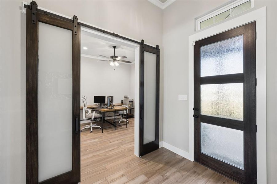Foyer with a barn door, crown molding, light wood-type flooring, and a ceiling fan