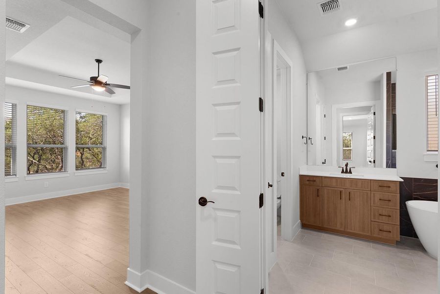 A well-lit bedroom with serene views of nature, adjoins a modern primary bathroom.