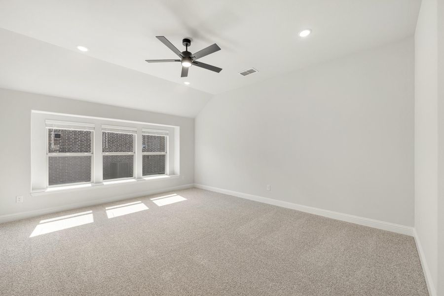 Empty bedroom with vaulted ceiling, ceiling fan, carpet flooring, and large triple window