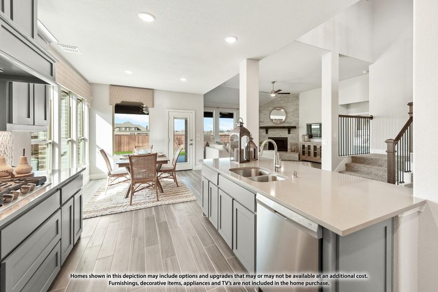 Open kitchen with gray cabinets, large island, and view into dining area and living room with stone fireplace. Open kitchen with gray cabinets, large island, and view into dining area and living room with stone fireplace.