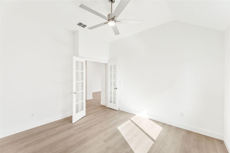 Empty room with vaulted ceiling, ceiling fan, French doors, and light hardwood floors Empty room with vaulted ceiling, ceiling fan, French doors, and light hardwood floors
