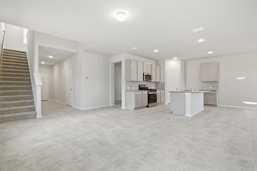 Image of a living room with tile flooring, light grey walls and a tan carpeted staircase leading upstairs