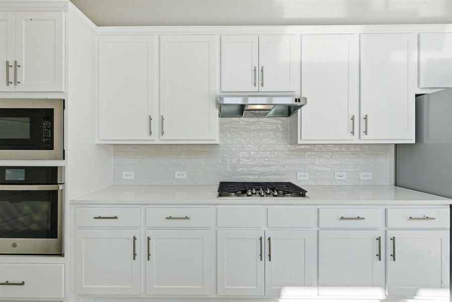 Kitchen featuring white cabinetry, appliances with stainless steel finishes, backsplash, and light stone countertops