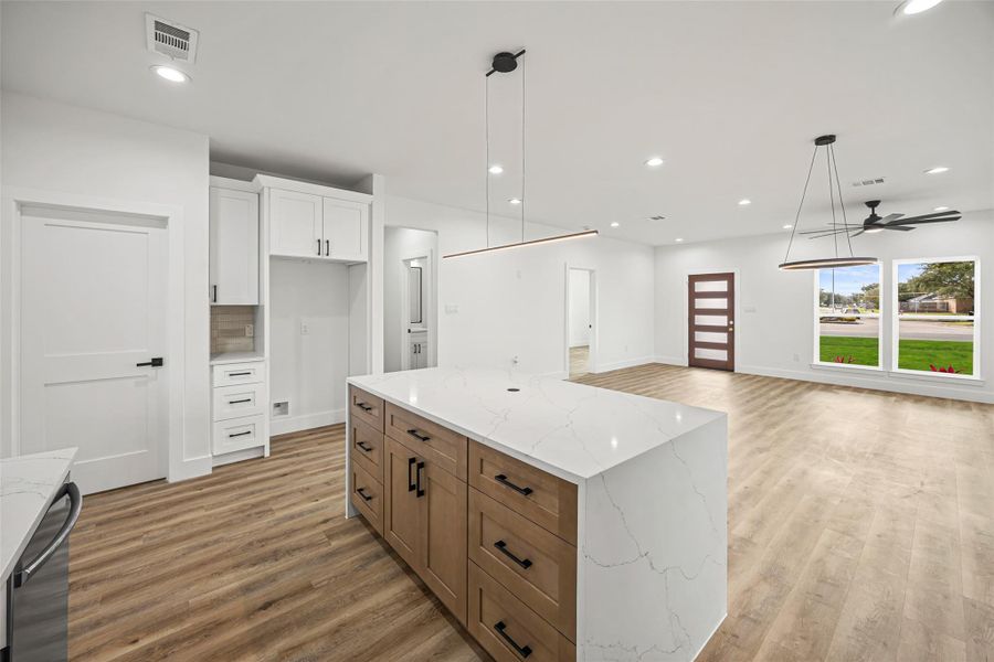 Large island with abundant storage, modern linear pendant lighting, and seamless flow into living space.