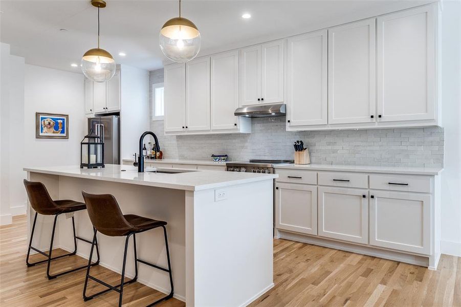 Kitchen with decorative backsplash, light wood-style flooring, white cabinets, hanging light fixtures, and appliances with stainless steel finishes Kitchen with decorative backsplash, light wood-style flooring, white cabinets, hanging light fixtures, and appliances with stainless steel finishes