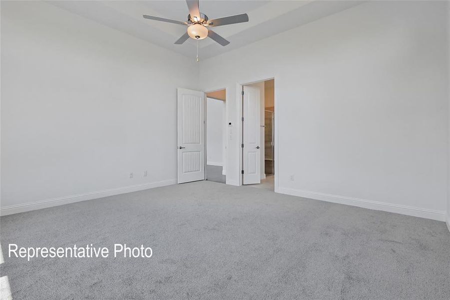Spacious room featuring light gray carpeting, crisp white walls, a tray ceiling, and a ceiling fan with integrated lighting