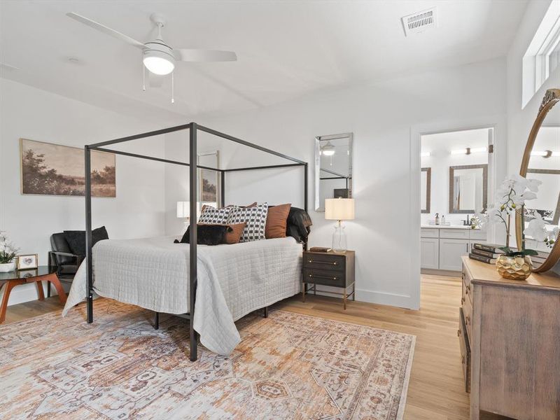 Bedroom featuring baseboards, visible vents, ensuite bathroom, and light wood-type flooring Bedroom featuring baseboards, visible vents, ensuite bathroom, and light wood-type flooring