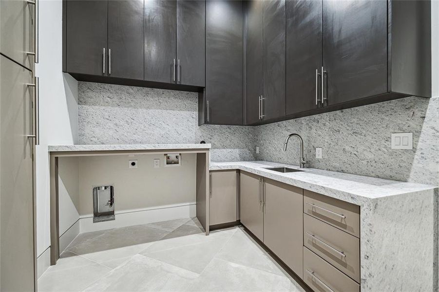 First floor utility room (1 of 2) is designed for both efficiency & style, and offers practical features such as a pull-out spray kitchen faucet and a single bowl kitchen sink, also accompanied by a PROFLO Drain Strainer for easy maintenance. The room exudes sophistication with its Harlem Caliza Porcelain Floor Tile and Crystallite Francini Quartzite countertops and backsplash, while washer and dryer connections offer convenience for everyday chores, making this space a functional and elegant addition.