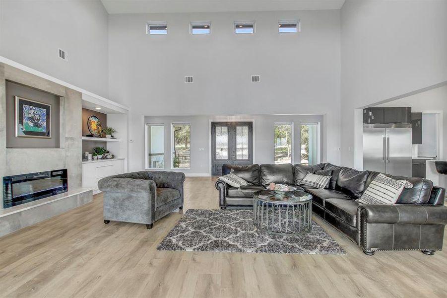 Living room featuring a fireplace, light wood-style flooring, plenty of natural light, built in features, and a towering ceiling