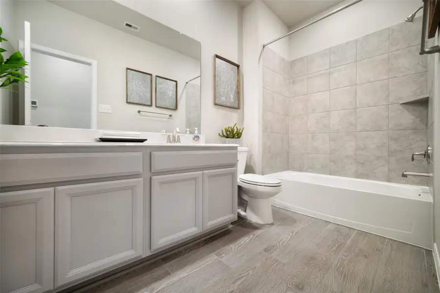 Secondary bath features tile flooring, bath/shower combo with tile surround, light stained wood cabinets, beautiful light countertop. Sample photo of completed home with similar floor plan. Actual colors and selections may vary.