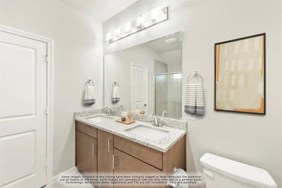 Bathroom with double sink vanity, granite countertop, wood cabinets, large mirror, and glass shower