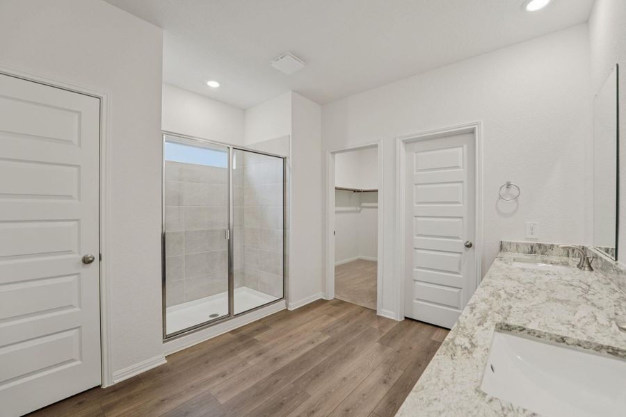Full bath with a walk in closet, double vanity, light wood-style floors, a stall shower, and recessed lighting