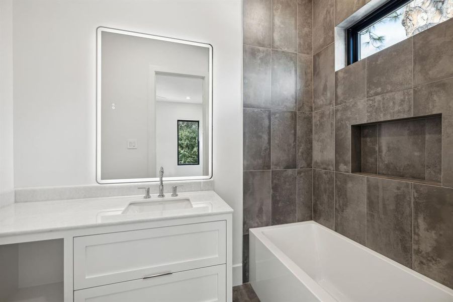 This secondary bathroom offers awhite vanity with a sleek marblecountertop. A large, illuminatedmirror adds a touch of luxury andexpands the sense of space. Thegray tile wall that extends up to theceiling adds a touch of warmth andtexture.