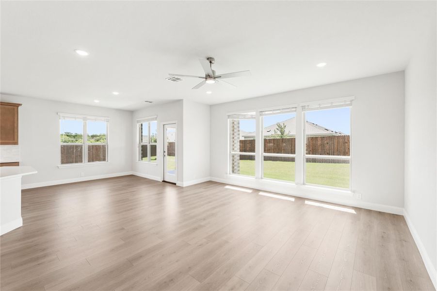 Open living room with light wood floors, ceiling fan, and large windows overlooking backyard