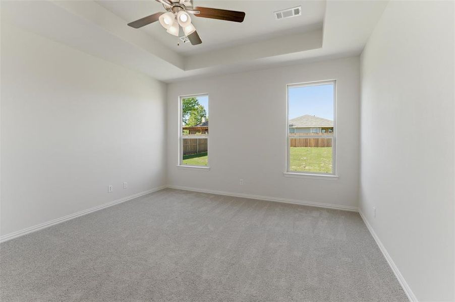 Empty room with light carpet, ceiling fan, and a raised ceiling