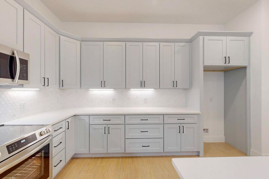Kitchen featuring stainless steel appliances, light wood-style flooring, white cabinets, and decorative backsplash