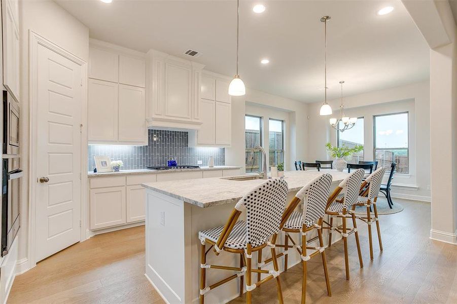 Kitchen with white cabinetry, decorative light fixtures, a kitchen island with sink, and sink