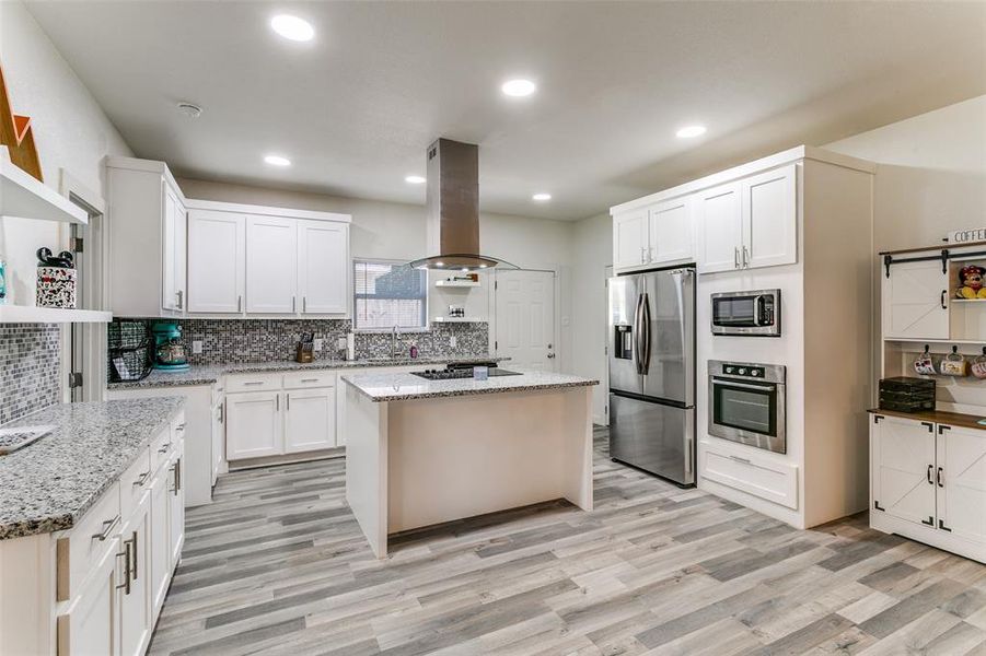Kitchen with a kitchen island, stainless steel appliances, white cabinets, decorative backsplash, and light stone countertops Kitchen with a kitchen island, stainless steel appliances, white cabinets, decorative backsplash, and light stone countertops