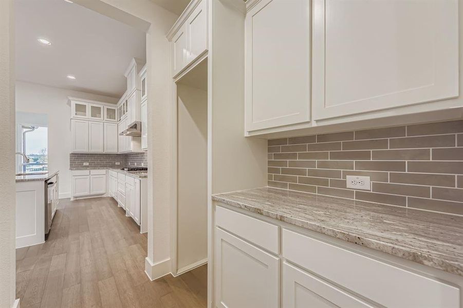 Kitchen featuring white cabinetry, light stone counters, tasteful backsplash, light wood-style floors, and glass insert cabinets Kitchen featuring white cabinetry, light stone counters, tasteful backsplash, light wood-style floors, and glass insert cabinets