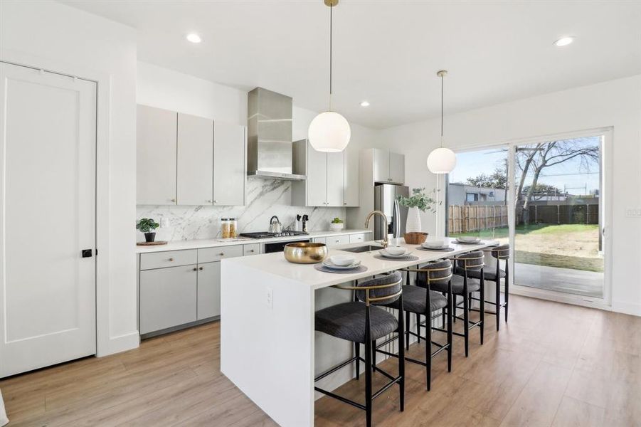 Kitchen with hanging light fixtures, a kitchen island with sink, sink, stainless steel appliances, and wall chimney exhaust hood