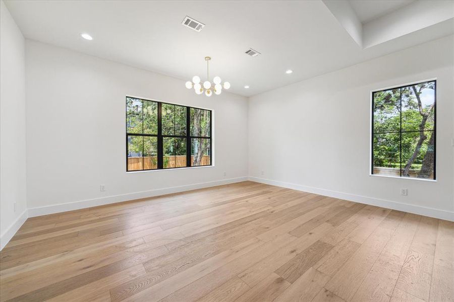 The formal dining room is highlighted by a designer gold and glass globe chandelier, complemented by designer neutral paint and recessed LED lighting. A large window bathes the room in natural light, creating a warm and inviting atmosphere.