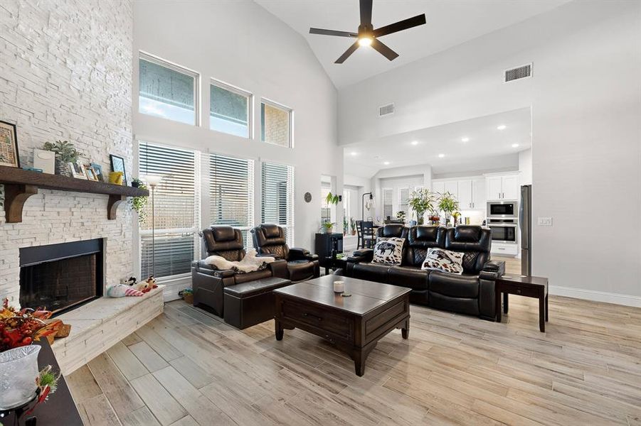 Living area with light wood-type flooring, a fireplace, ceiling fan, high vaulted ceiling, and recessed lighting Living area with light wood-type flooring, a fireplace, ceiling fan, high vaulted ceiling, and recessed lighting