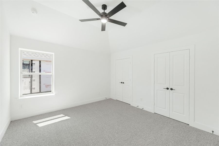 Empty bedroom with gray carpet, ceiling fan, double closet doors, and a window Empty bedroom with gray carpet, ceiling fan, double closet doors, and a window