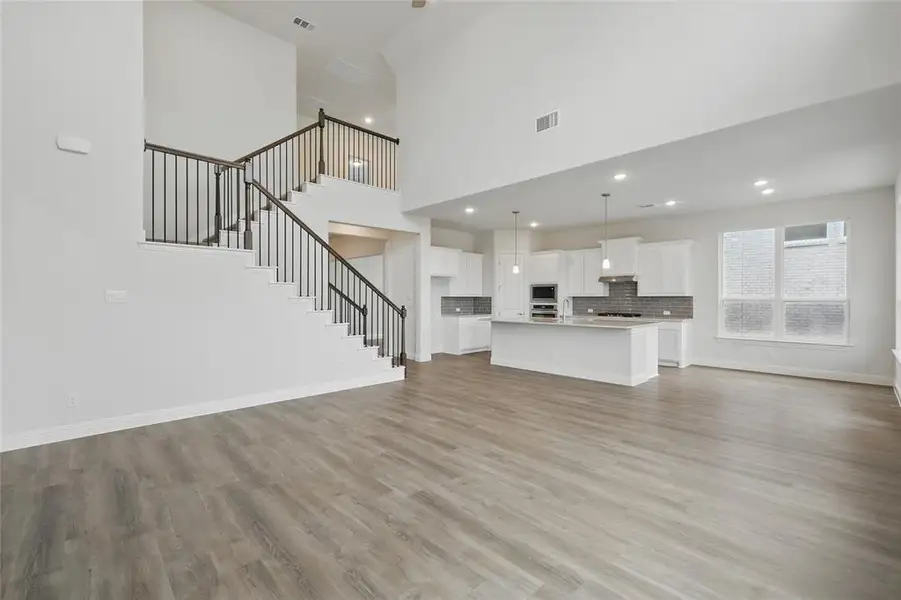 Unfurnished living room featuring baseboards, light wood-type flooring, visible vents, and stairway