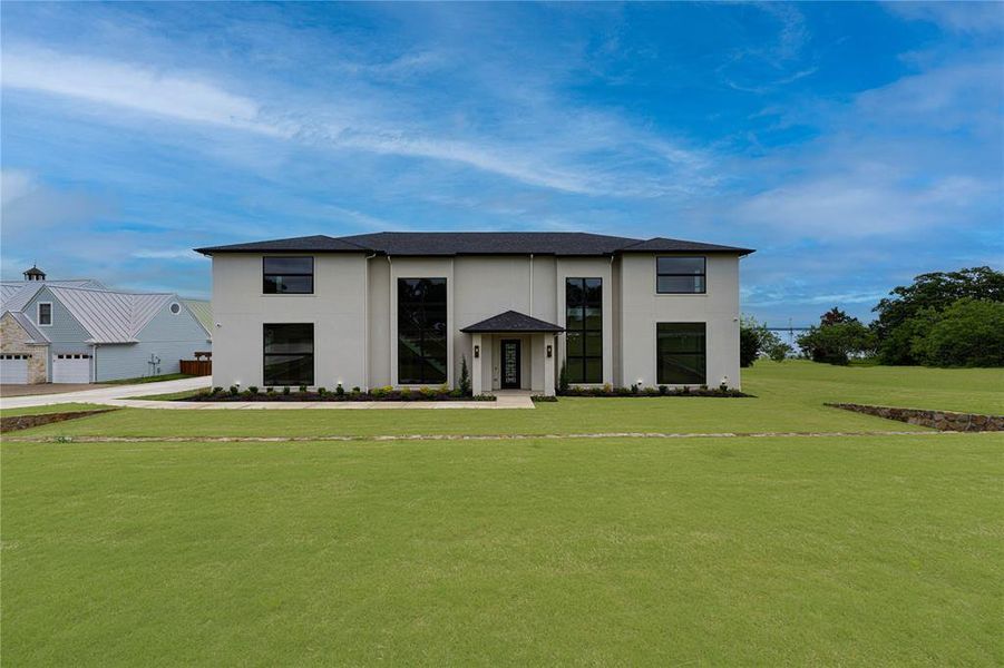 Modern home with a front yard, stucco siding, and a shingled roof