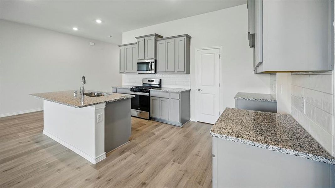 Kitchen featuring gray cabinetry, light stone countertops, an island with sink, stainless steel appliances, and recessed lighting