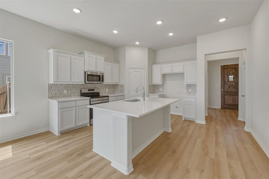 Kitchen featuring a large central island with a sink, white cabinetry, stainless steel appliances, a tiled backsplash, and wood-finish flooring
