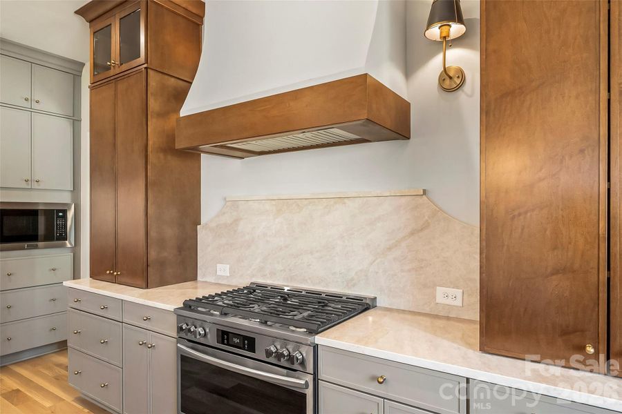 This centerpiece that anchors the space is a custom hood with side lighting, a 6 burner gas stove and quartz backsplash.