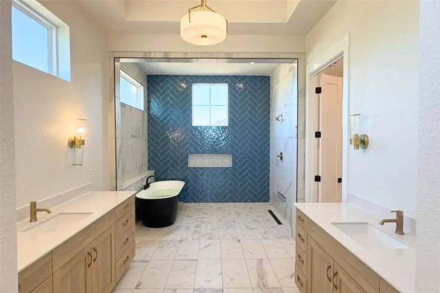 Bathroom featuring a soaking tub, a walk in shower, two vanities, and a tray ceiling