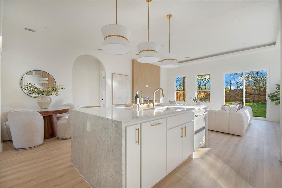 Kitchen featuring white cabinets, light stone countertops, open floor plan, decorative light fixtures, and light wood-style flooring Kitchen featuring white cabinets, light stone countertops, open floor plan, decorative light fixtures, and light wood-style flooring