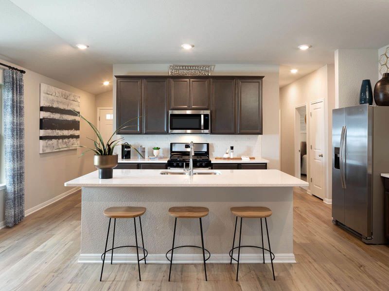 Kitchen featuring appliances with stainless steel finishes, dark brown cabinetry, tasteful backsplash, light wood-style flooring, and light countertops