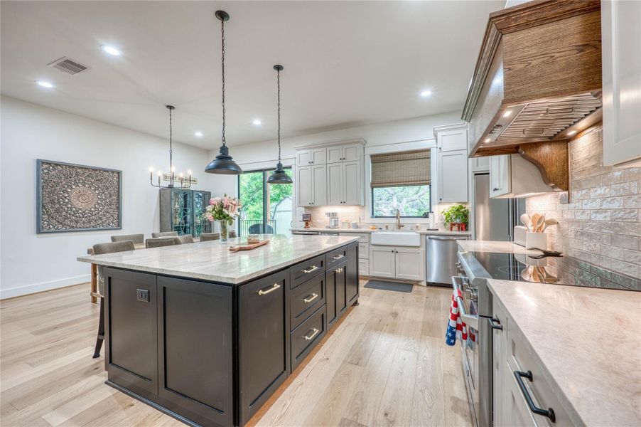 Kitchen featuring a large central island with seating, pendant lighting, stainless steel appliances, a farmhouse sink, and wood-finish flooring