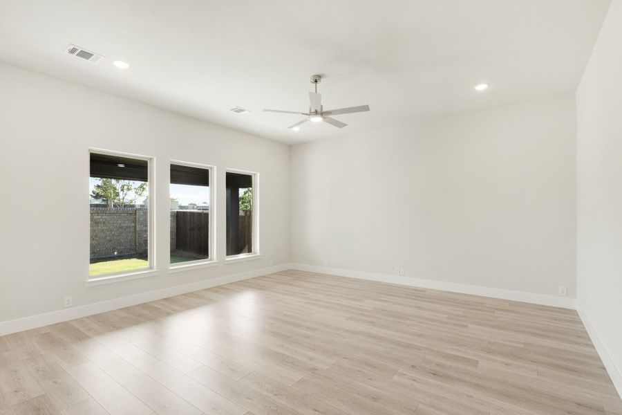 Empty room with light wood floors, ceiling fan, recessed lighting, and three windows overlooking a fenced backyard Empty room with light wood floors, ceiling fan, recessed lighting, and three windows overlooking a fenced backyard