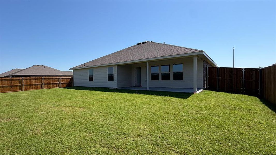 Expansive fenced backyard featuring a covered patio, neutral-toned siding, a dark shingle roof, and multiple windows Expansive fenced backyard featuring a covered patio, neutral-toned siding, a dark shingle roof, and multiple windows